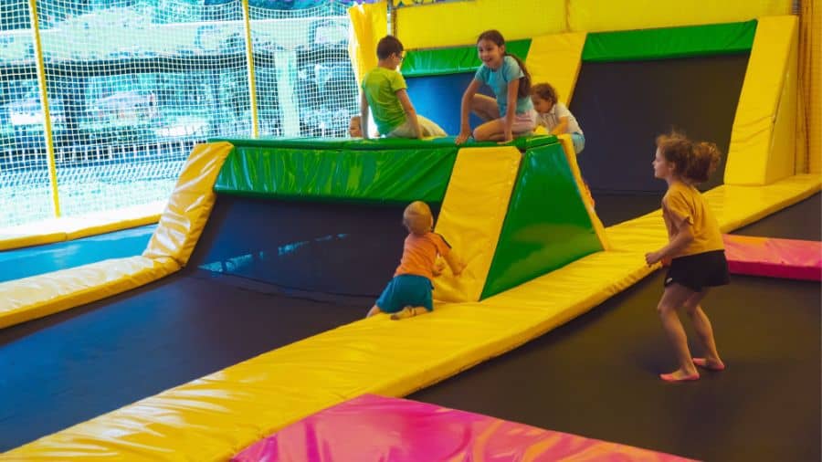 Children play at a vibrant trampoline park, bouncing on colorful indoor trampolines with padded walls and nets for safety.