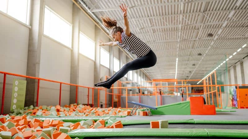 A person jumps into a foam pit at an indoor trampoline park, enjoying fitness benefits, surrounded by orange netting and soft blocks.