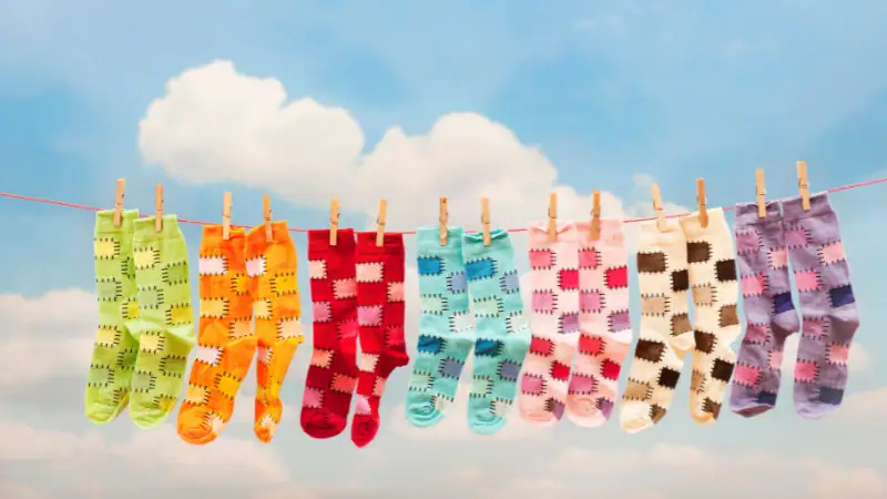 Colorful knitted socks hanging on a clothesline against a blue sky with clouds.
