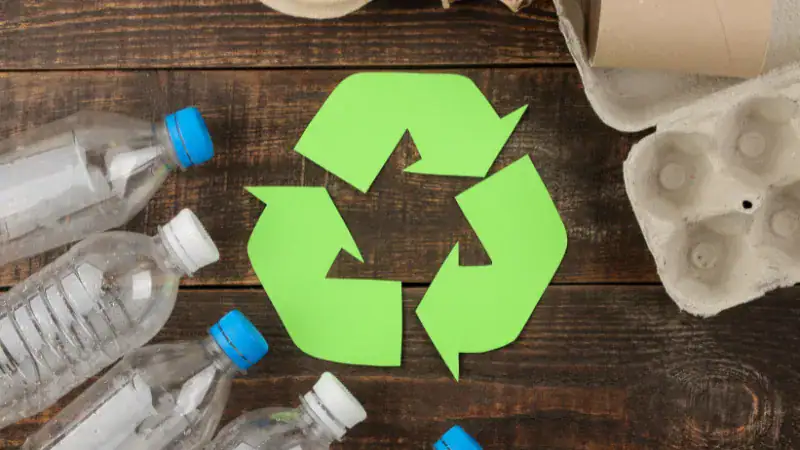 Recycling symbol on wooden surface surrounded by plastic bottles and egg carton, emphasizing eco-friendly waste management and sustainable practices.