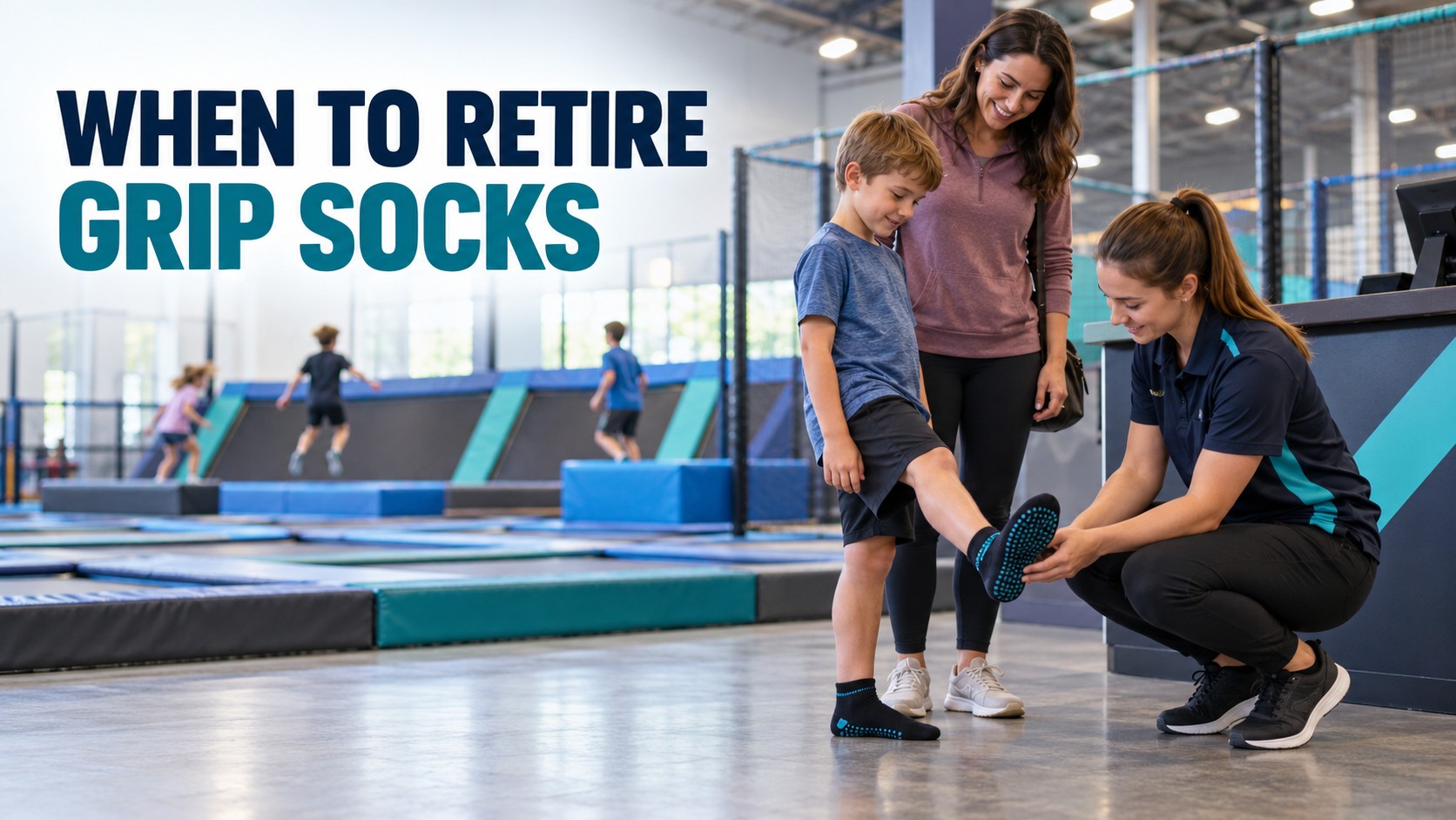 A staff member helping a young boy try on grip socks at an indoor trampoline park, with other children jumping in the background.