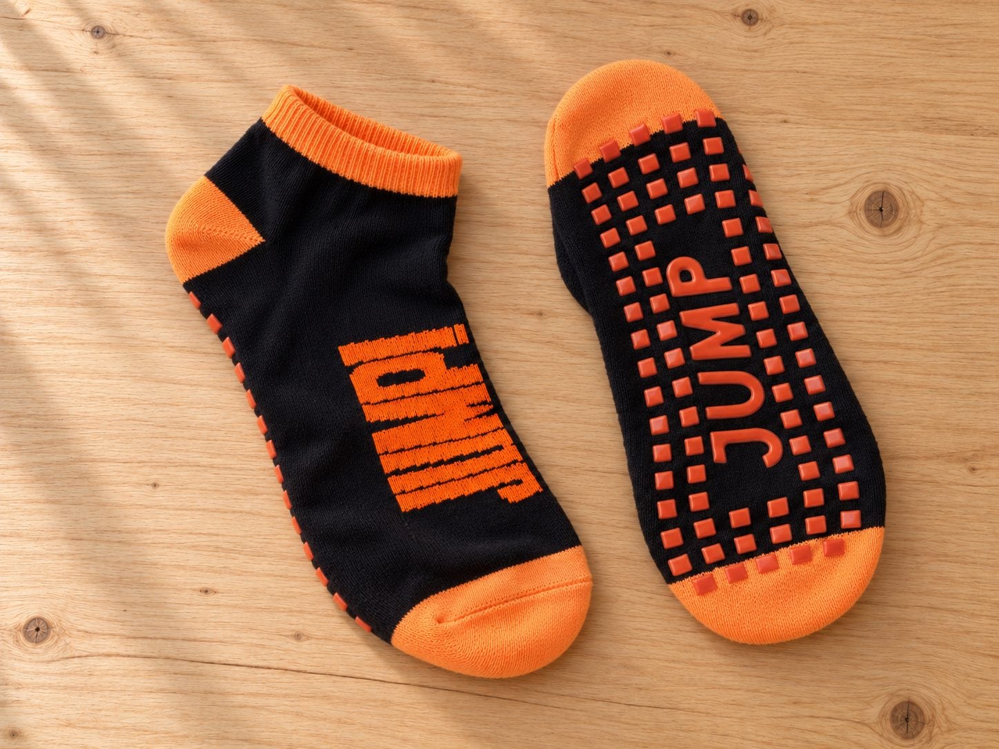 Black and orange custom logo trampoline grip socks with JUMP branding laid flat on a wooden table